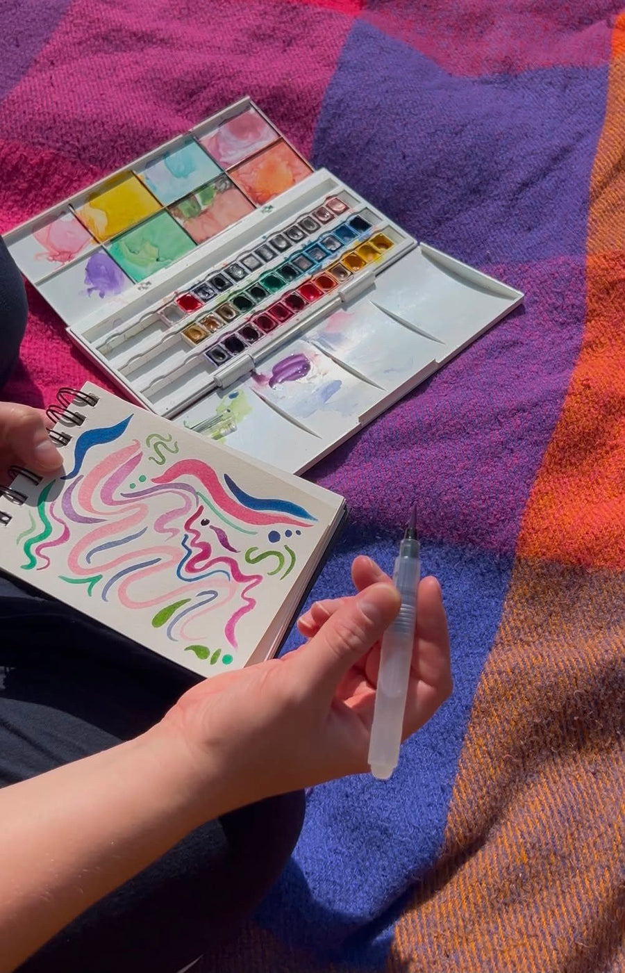 Watercolour paints and a painted card on a picnic blanket at a creative women's meet-up